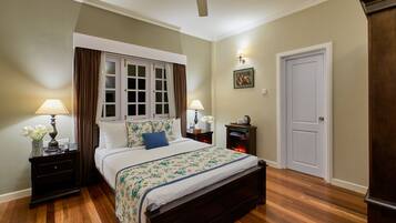 A neatly arranged bedroom with a large bed, two bedside tables with lamps, a nightstand, a door, and a ceiling fan.