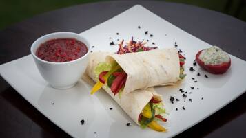A plate with a wrap, a bowl of sauce, and a stuffed tomato.