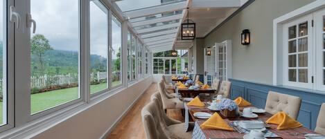 A conservatory with a dining area, large windows, and a view of the outdoors.