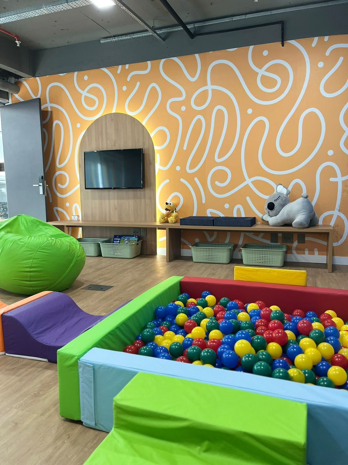 A play area with a ball pit, bean bags, and a TV on the wall.