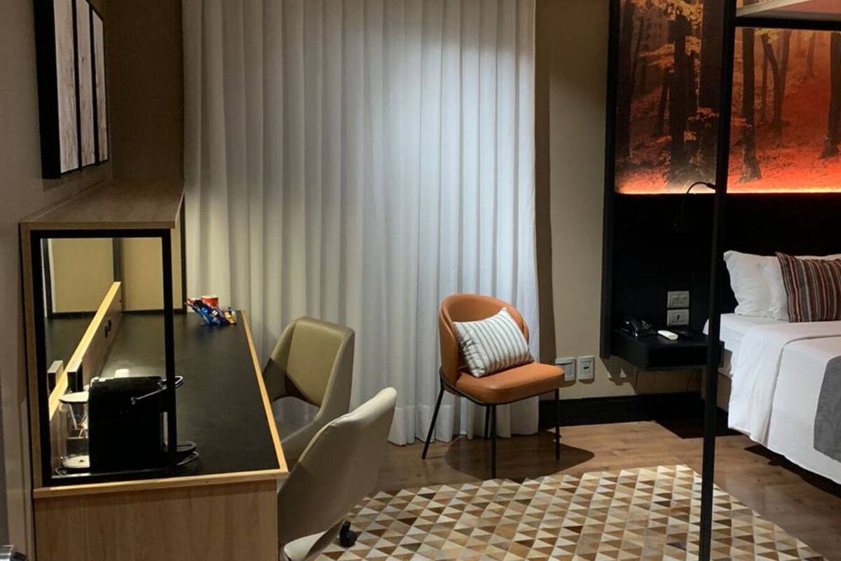 Habitación de hotel con cama, escritorio, silla y una ventana grande con vista al bosque.