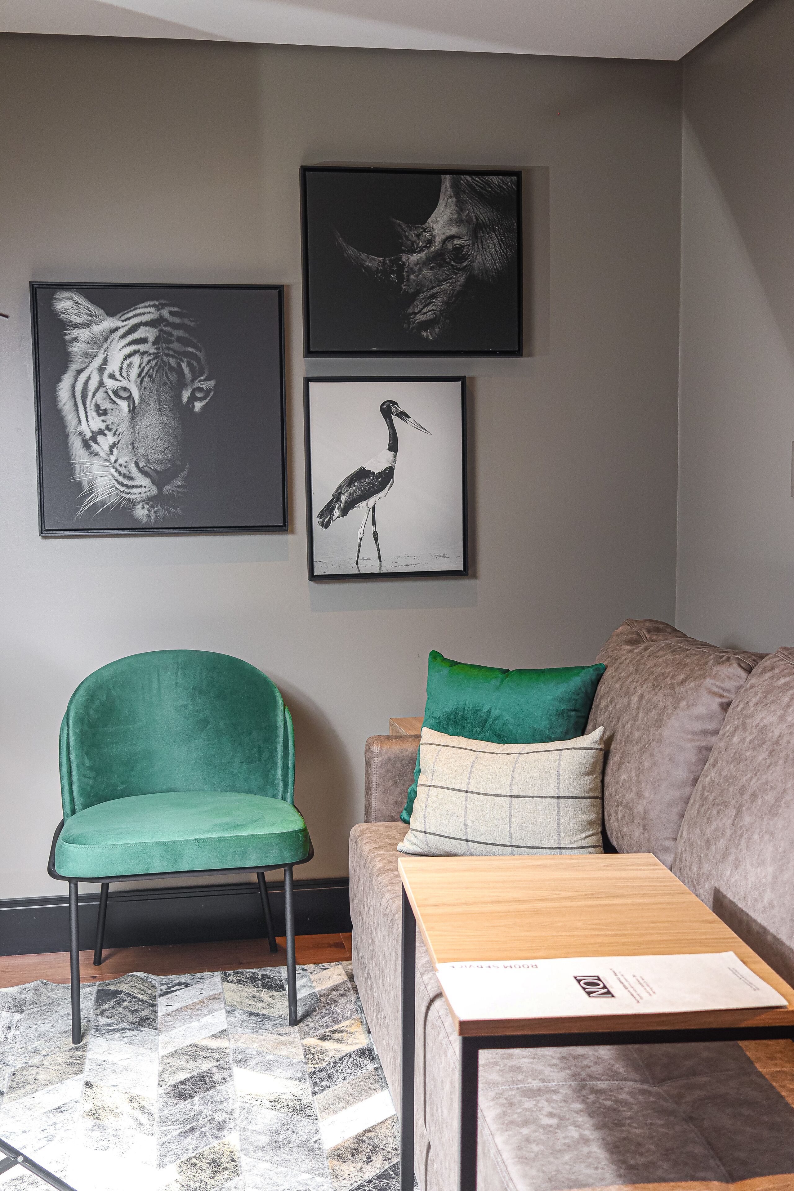 Una sala de estar con un sillón verde, un sofá gris y una mesa de centro de madera. Hay tres grabados enmarcados de animales en la pared.