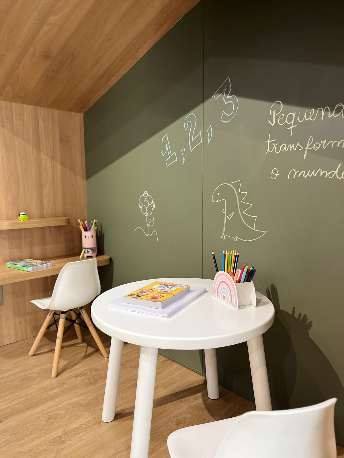 Une pièce avec une table blanche, une chaise blanche et un mur recouvert d’un tableau noir sur lequel on a dessiné et écrit des chiffres.