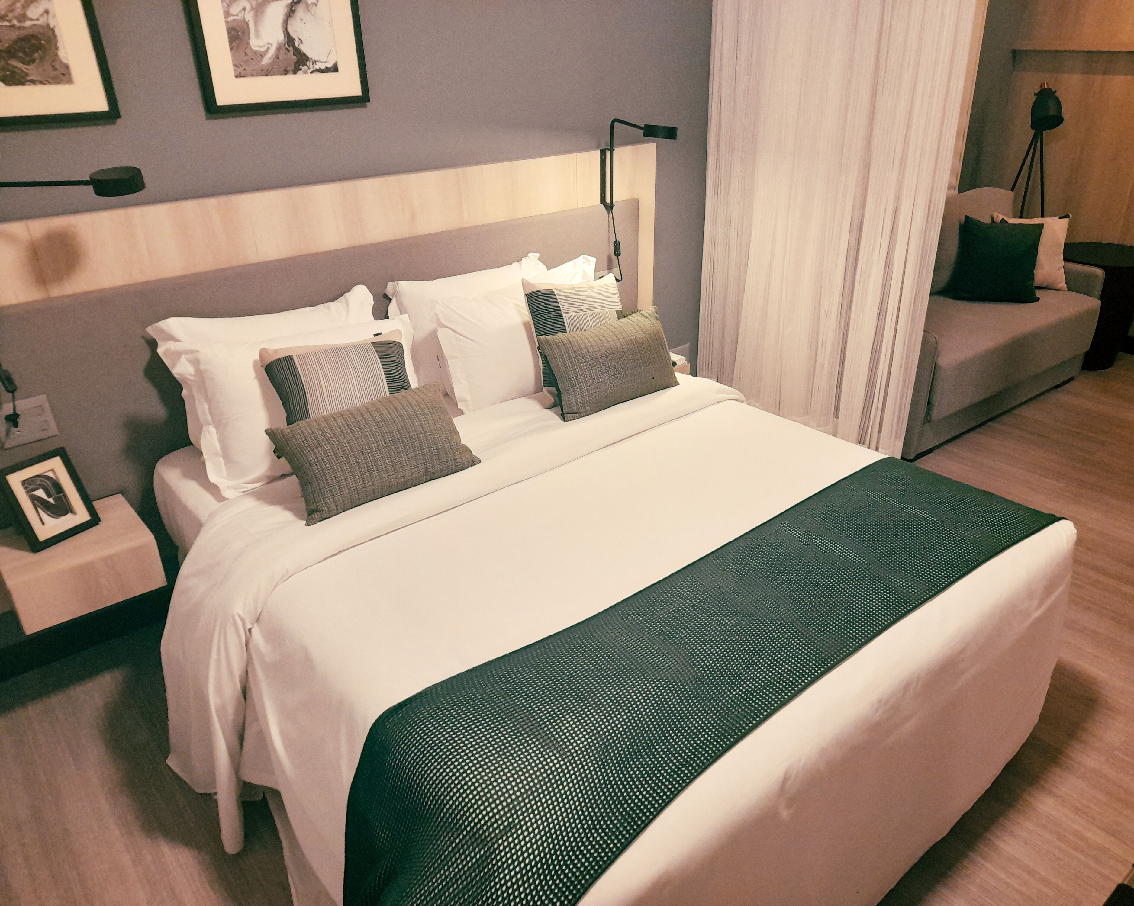A neatly made bed with white linens and a green accent, a bedside table with a lamp, and a framed picture on the wall.