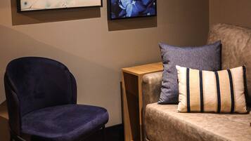 Una habitación con una silla azul, un sofá beige con almohadones a rayas y tres obras de arte enmarcadas en la pared.