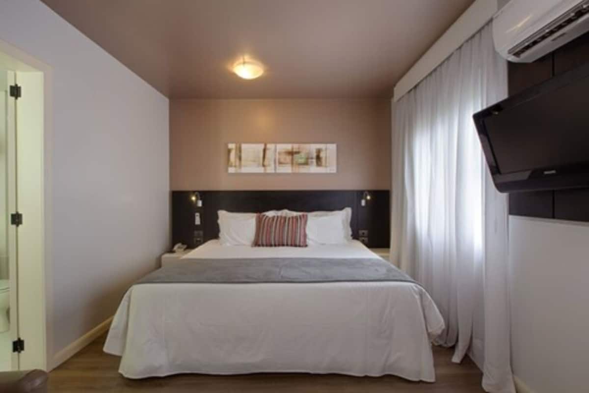 Un dormitorio con una cama, cabecera, televisor de pared y una lámpara en el techo.