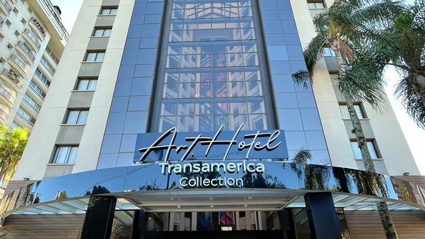 Entrada de hotel com design moderno, destacando uma grande fachada de vidro e uma placa bem visível para o Art Hotel Transamerica Collection.