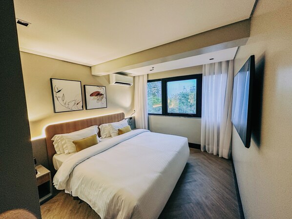 Habitación de hotel con una cama grande, un televisor de pantalla plana en la pared y una ventana con cortinas.