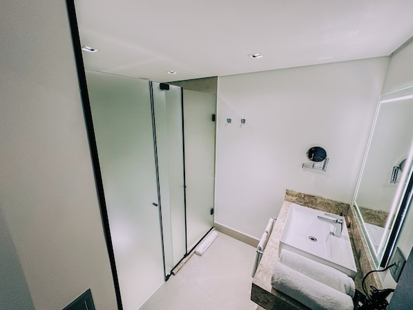 A modern bathroom with a glass shower enclosure, a white sink with a marble countertop, and a large mirror.