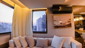 Sala de estar moderna com sofá seccional, uma janela grande com vista para a cidade e ar condicionado instalado.