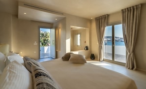 Een ruime slaapkamer met een groot bed, een balkon met uitzicht op zee, en een deur naar een terras.