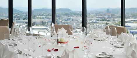 Mesa dispuesta para una comida con vista a la ciudad a través de amplios ventanales.