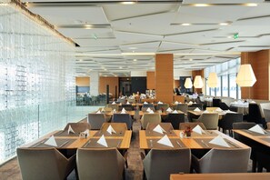 Ein moderner Hotel-Speisebereich mit mehreren Tischen und Stühlen, einer Glaswand und großen Fenstern.