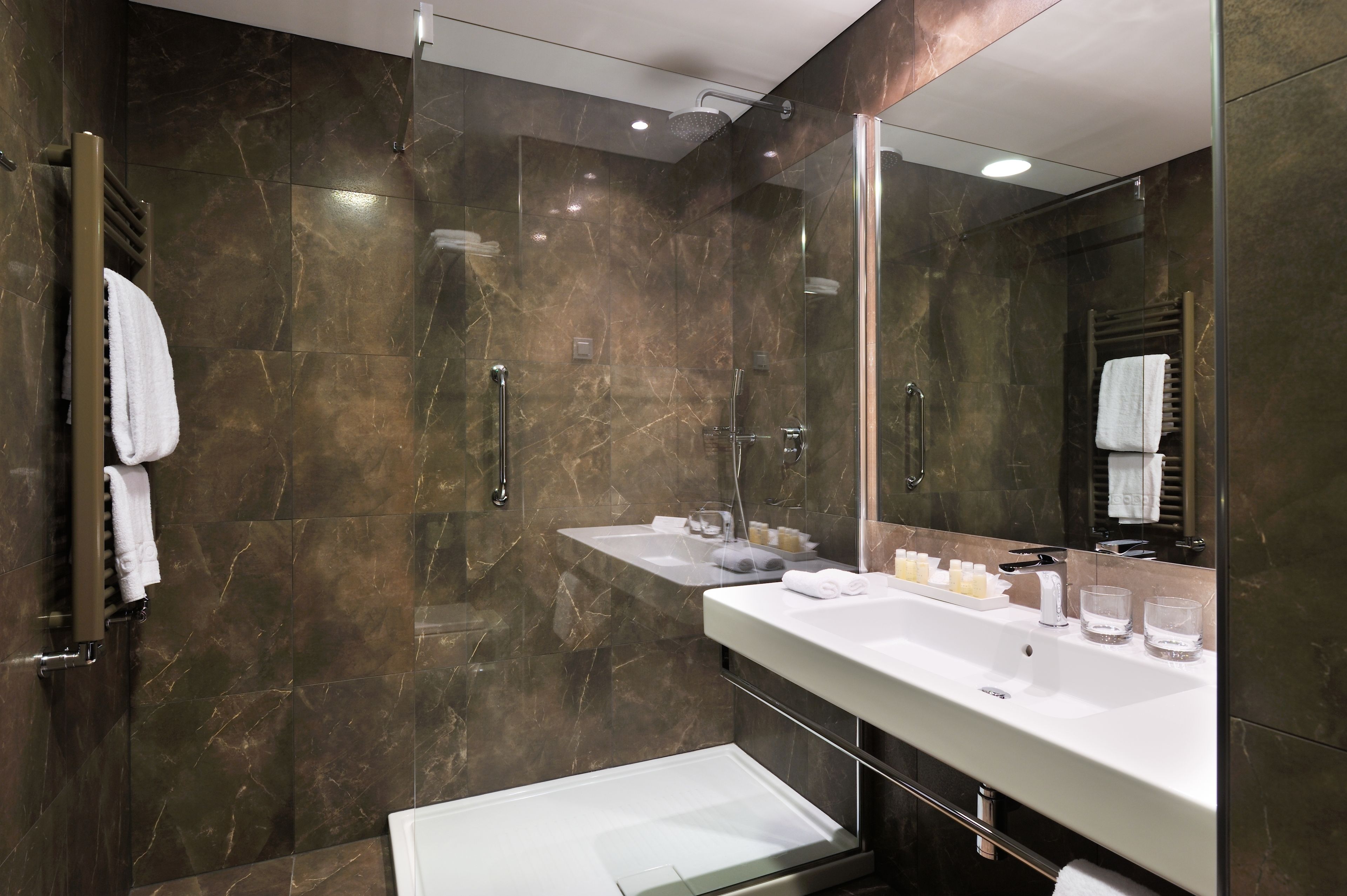 A modern bathroom with a glass-enclosed shower, a large vanity with a mirror, and marble walls.