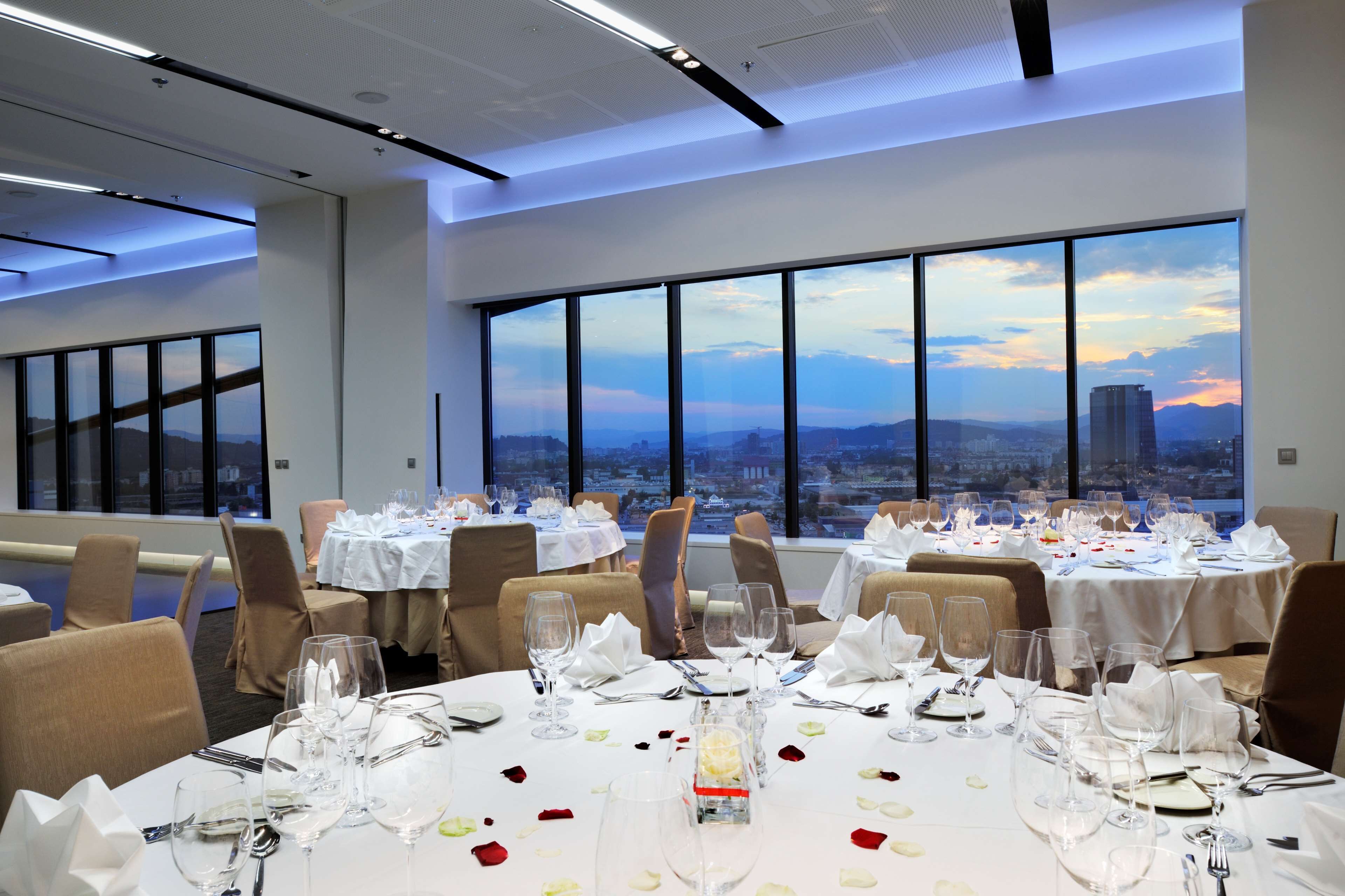 A dining area with tables set for a meal, large windows offering a city view, and a modern interior design.
