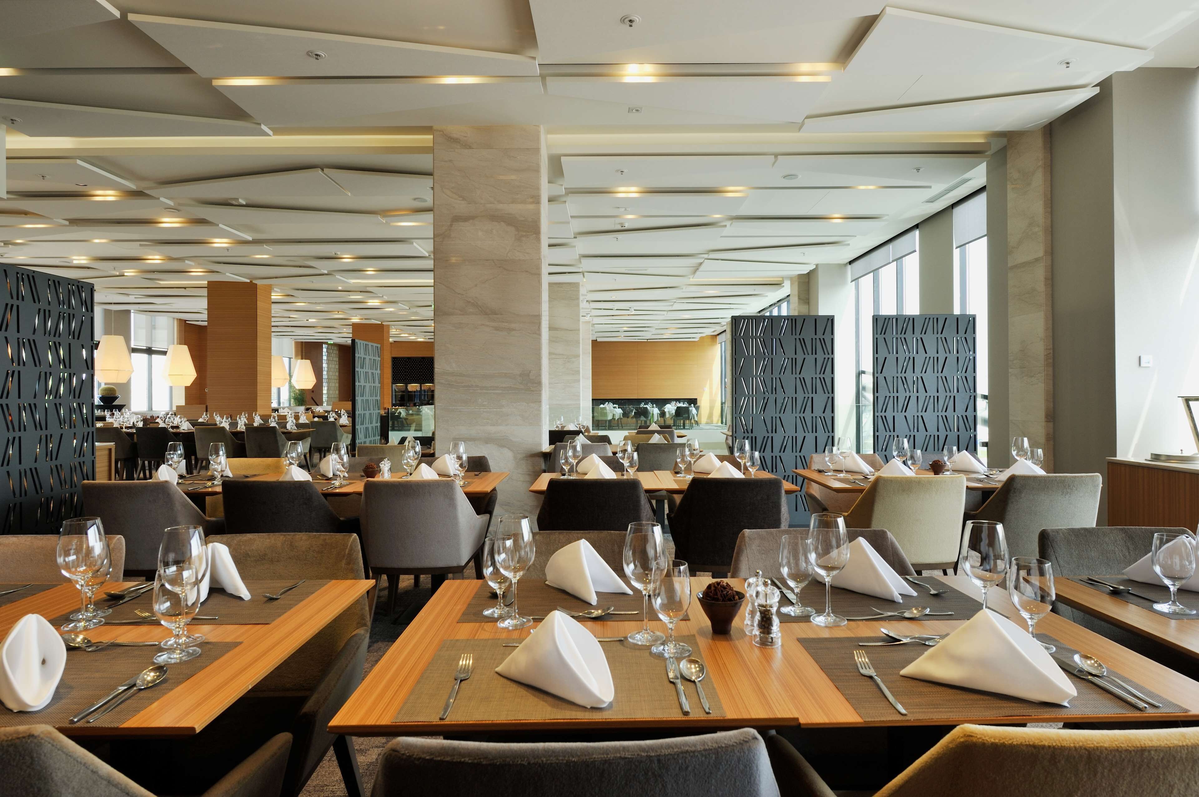 Un restaurante moderno con varias mesas de comedor, cada una dispuesta con servilletas blancas, cubiertos y copas de vino.