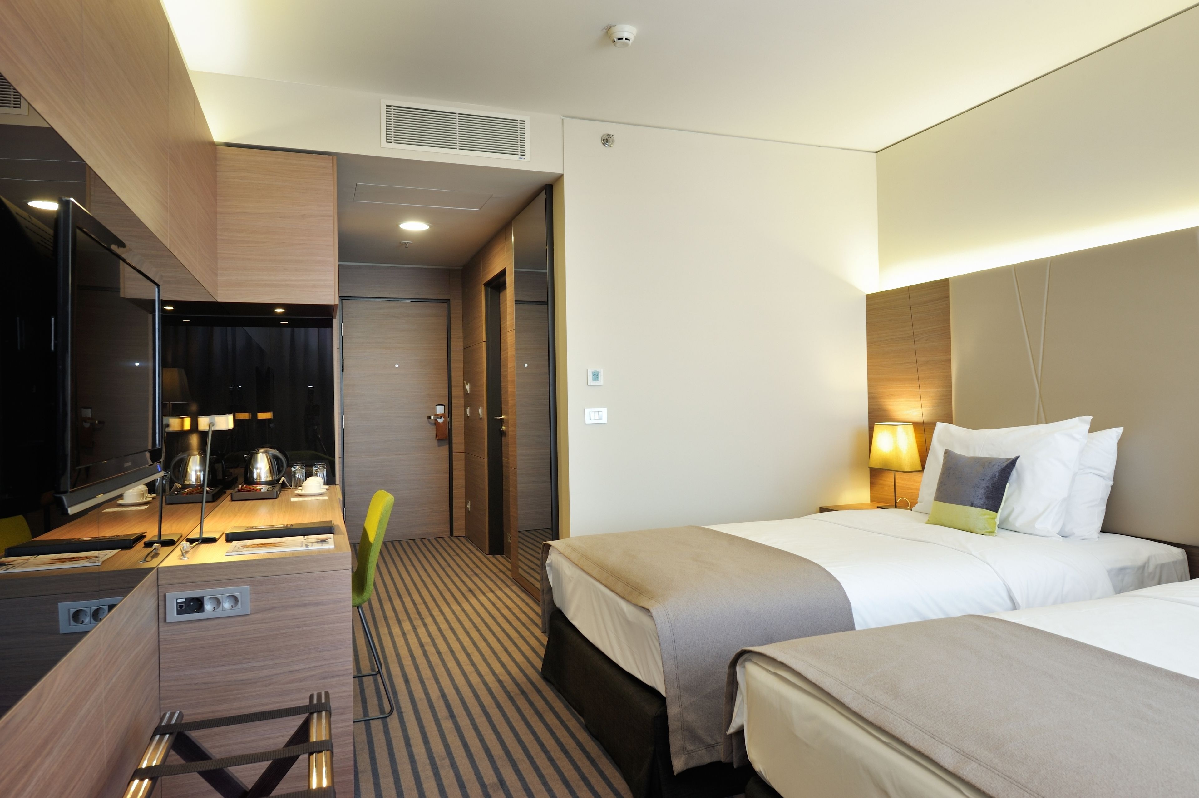 A hotel room with two beds, a desk with a mirror, a sink, and a shower area.