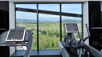 A gym with two treadmills and a large window offering a view of a green landscape and mountains.