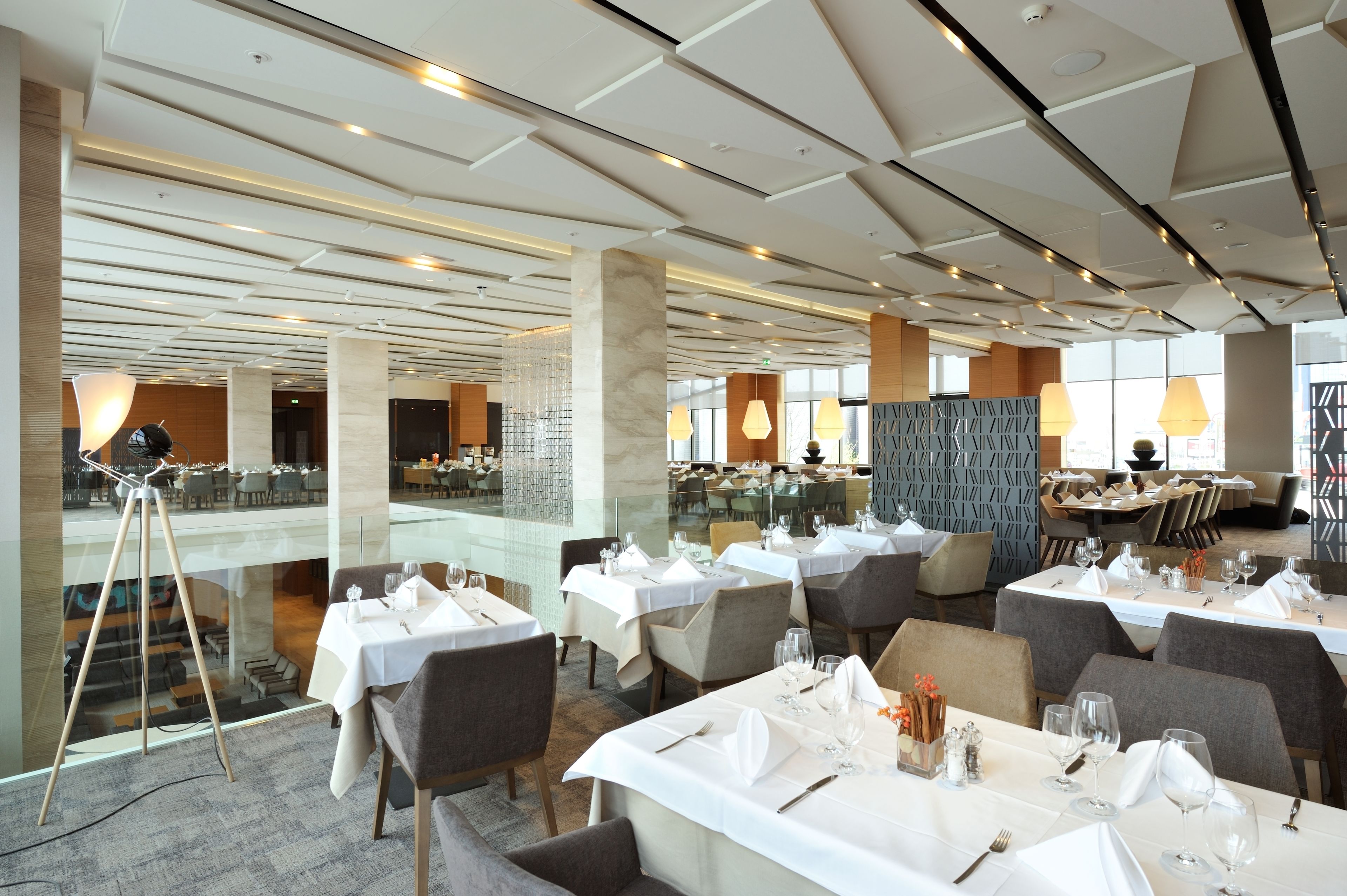 A spacious dining area with multiple tables set for guests, large windows providing natural light, and a modern ceiling design.
