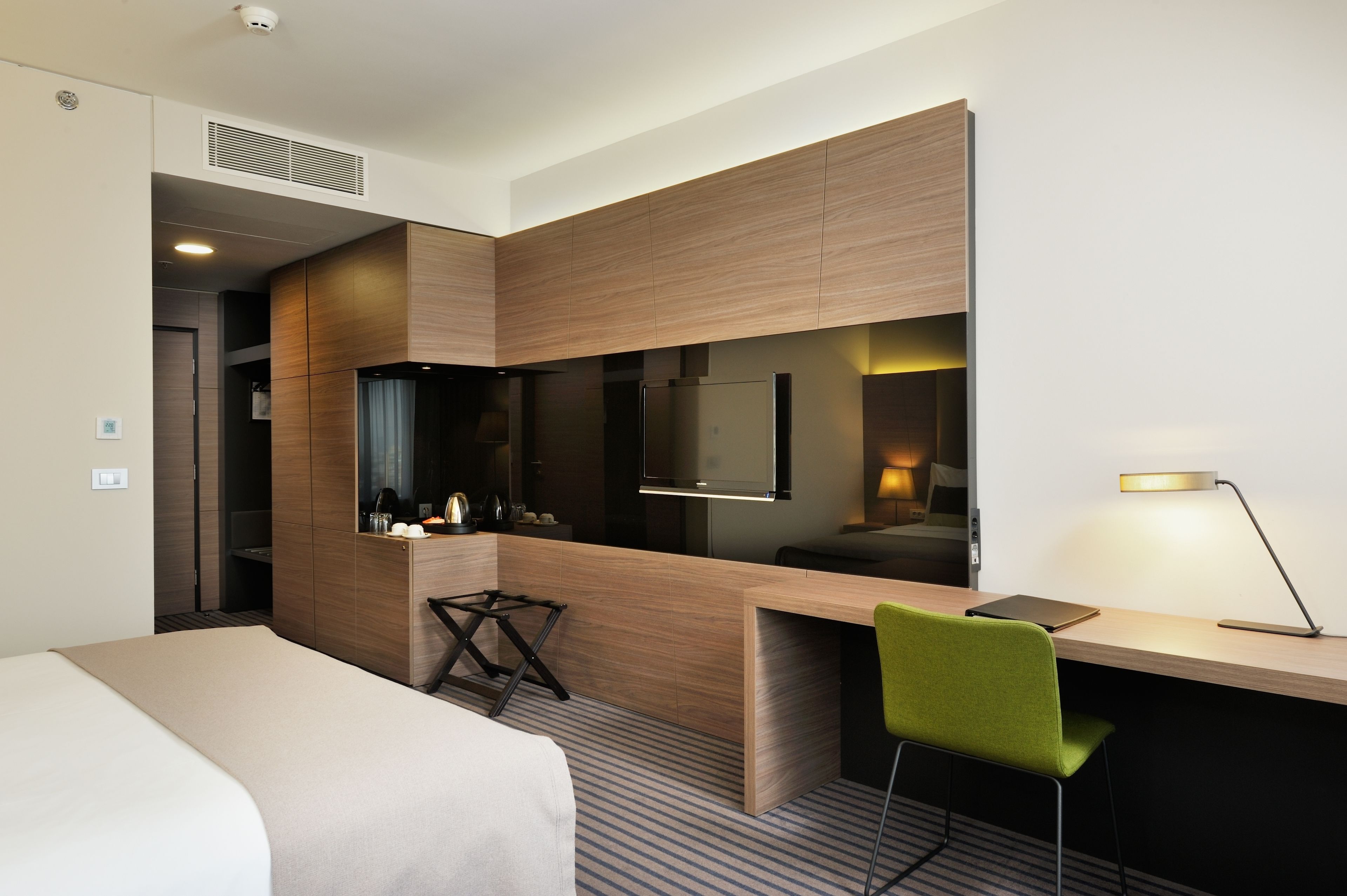 Une chambre d’hôtel moderne équipée d’un lit, d’un bureau avec une chaise, d’un téléviseur à écran plat et d’un miroir.
