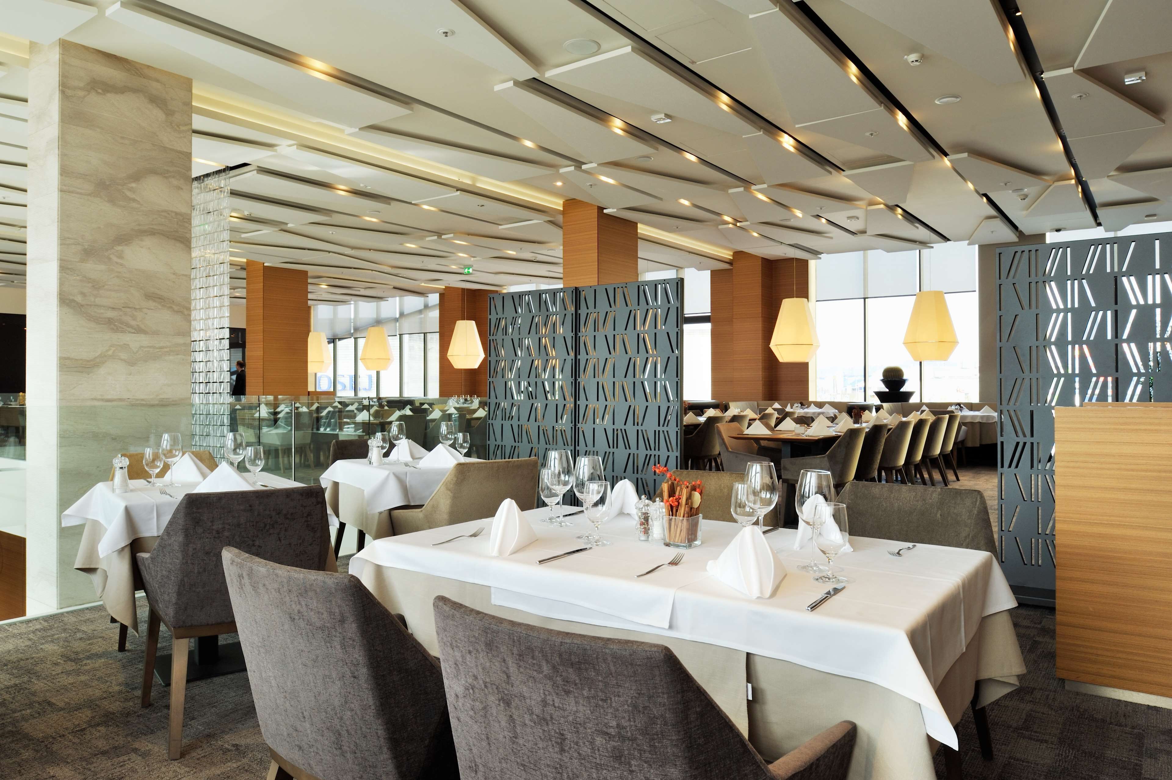 Un restaurante con mesas dispuestas para comer, que presenta un interior moderno con techo alto e iluminación colgante.