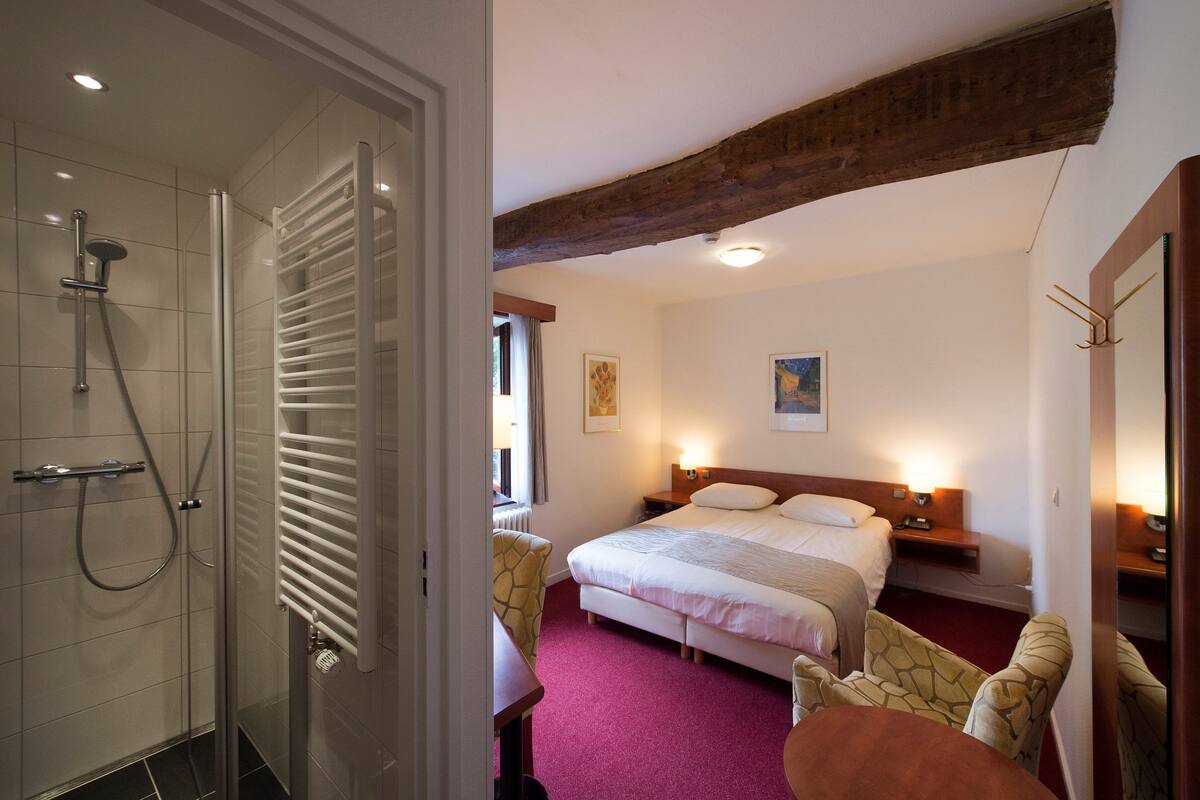 A hotel room with a shower, bed, bedside tables, and a dining area.