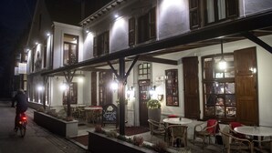 A traditional building with a covered outdoor seating area, multiple windows, and a sign indicating it is a restaurant.