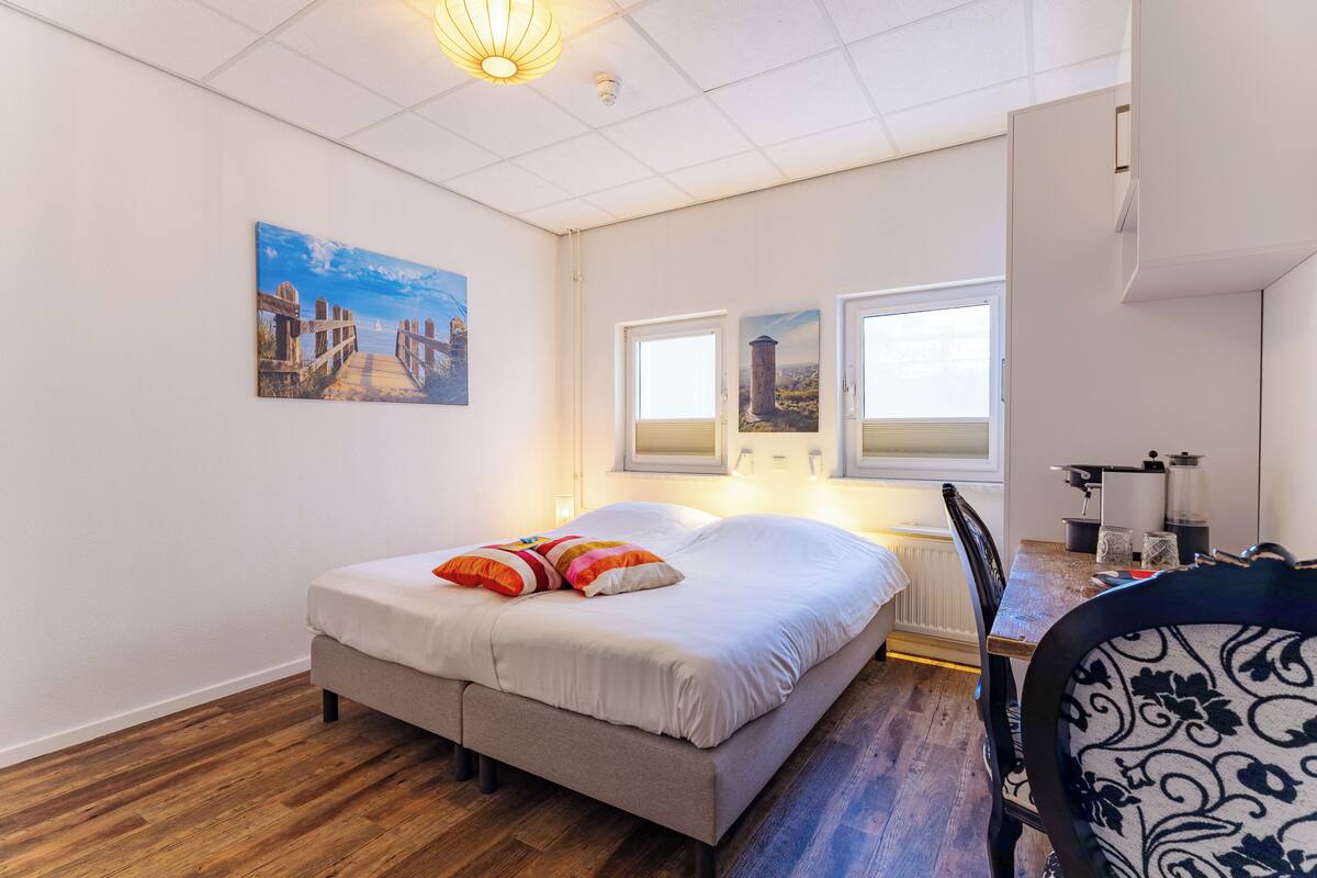 A bedroom with a bed, a desk, and two windows.
