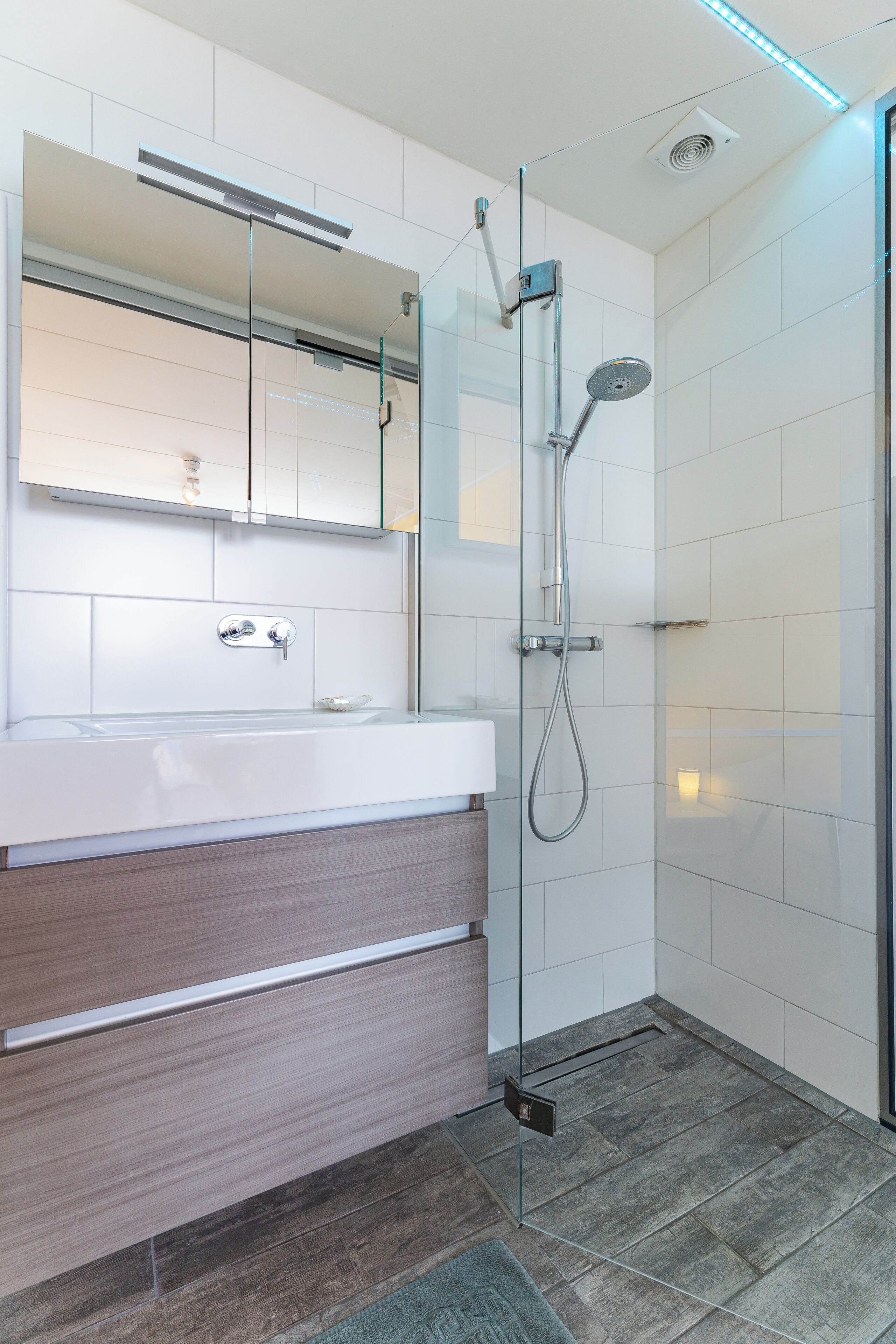 Een moderne badkamer met een douchecabine van glas, een witte wastafel met houten meubel en een spiegel erboven.