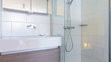 Een moderne badkamer met een douchecabine van glas, een witte wastafel met houten meubel en een spiegel erboven.