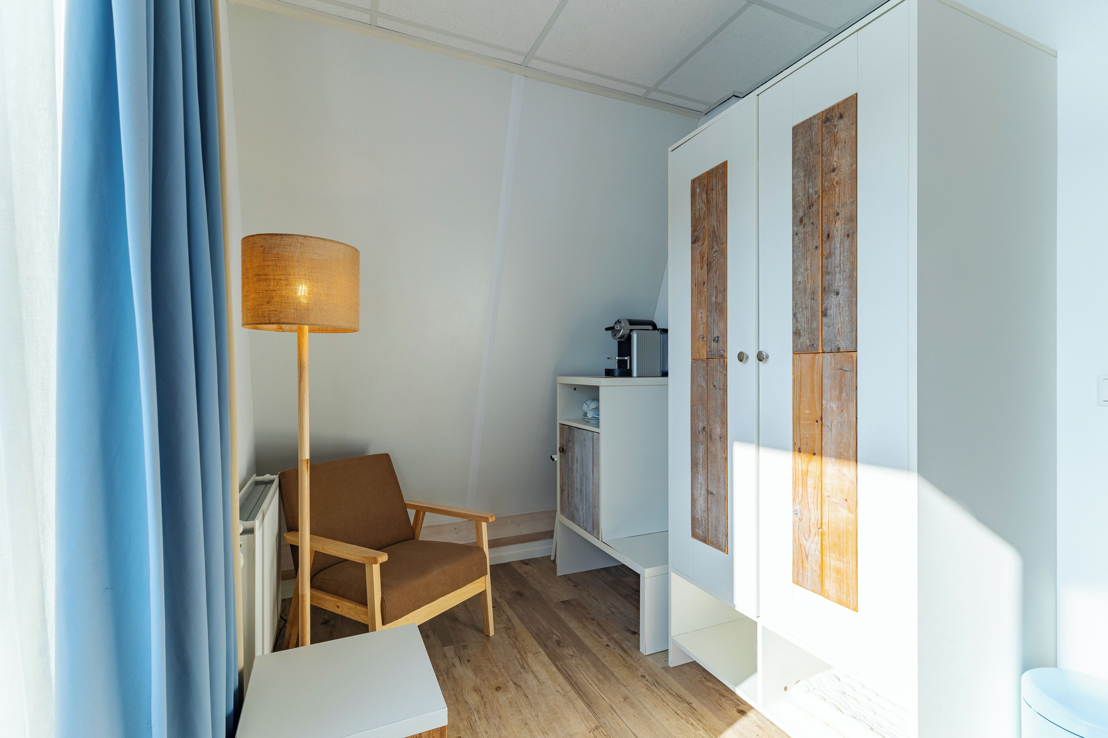 Een kamer met een houten stoel, een witte tafel, een vloerlamp en een garderobe met houten panelen.