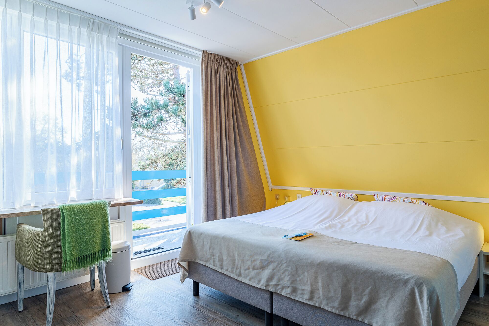 Quarto com cama, cadeira, janela com cortinas e vista para o exterior.