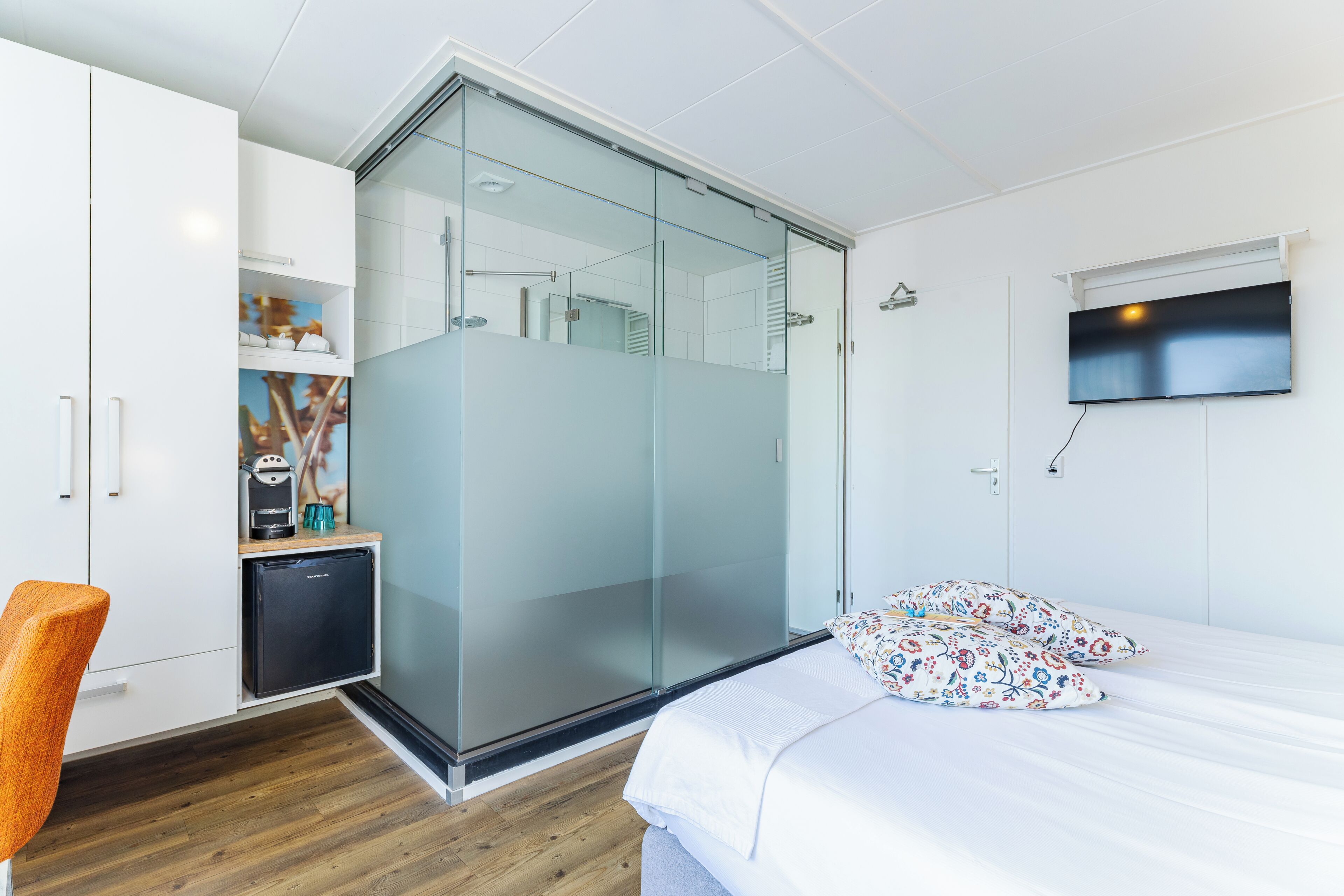 Un dormitorio con cama, televisión, armario, nevera pequeña y zona de ducha.