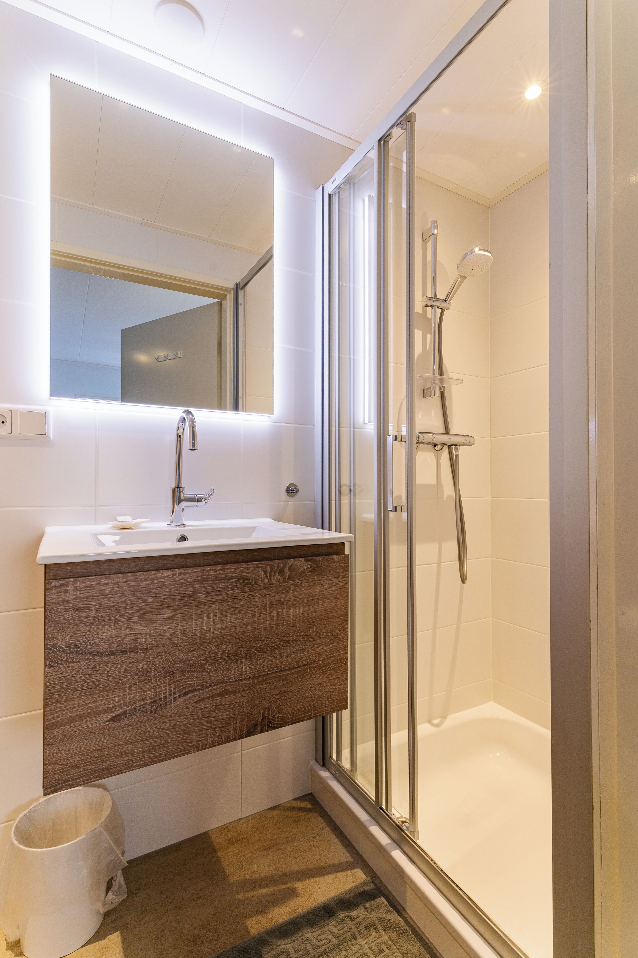 Een moderne badkamer met een glazen douchecabine, een houten wastafelmeubel en een grote spiegel.