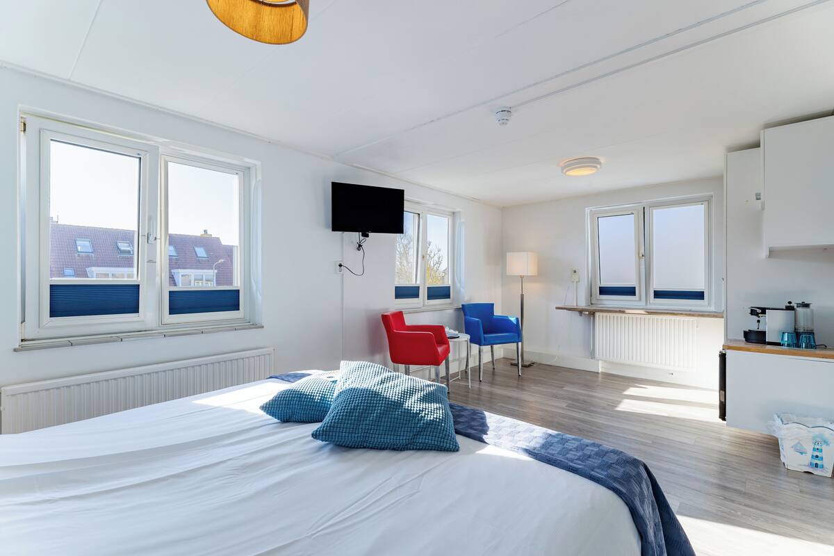 A modern hotel room with a large bed, two chairs, a TV, and a view of buildings outside.