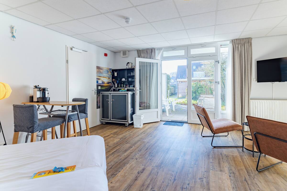 A hotel room with a bed, a desk, a chair, a kitchenette, and a TV.