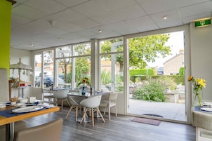 Ein moderner Essbereich mit Glaswand, Holzboden und Blick auf Garten und umliegende Gebäude.