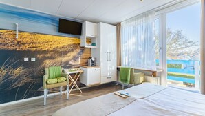 A modern hotel room with a large bed, a flat-screen TV mounted on the wall, a small desk with a chair, and a view of the outside. - Hotel Kijkduin (Domburg)