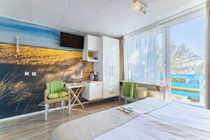 Ein modernes Hotelzimmer mit einem großen Bett, einem flachbildfernseher an der Wand, einem kleinen Schreibtisch mit Stuhl und Blick ins Freie.