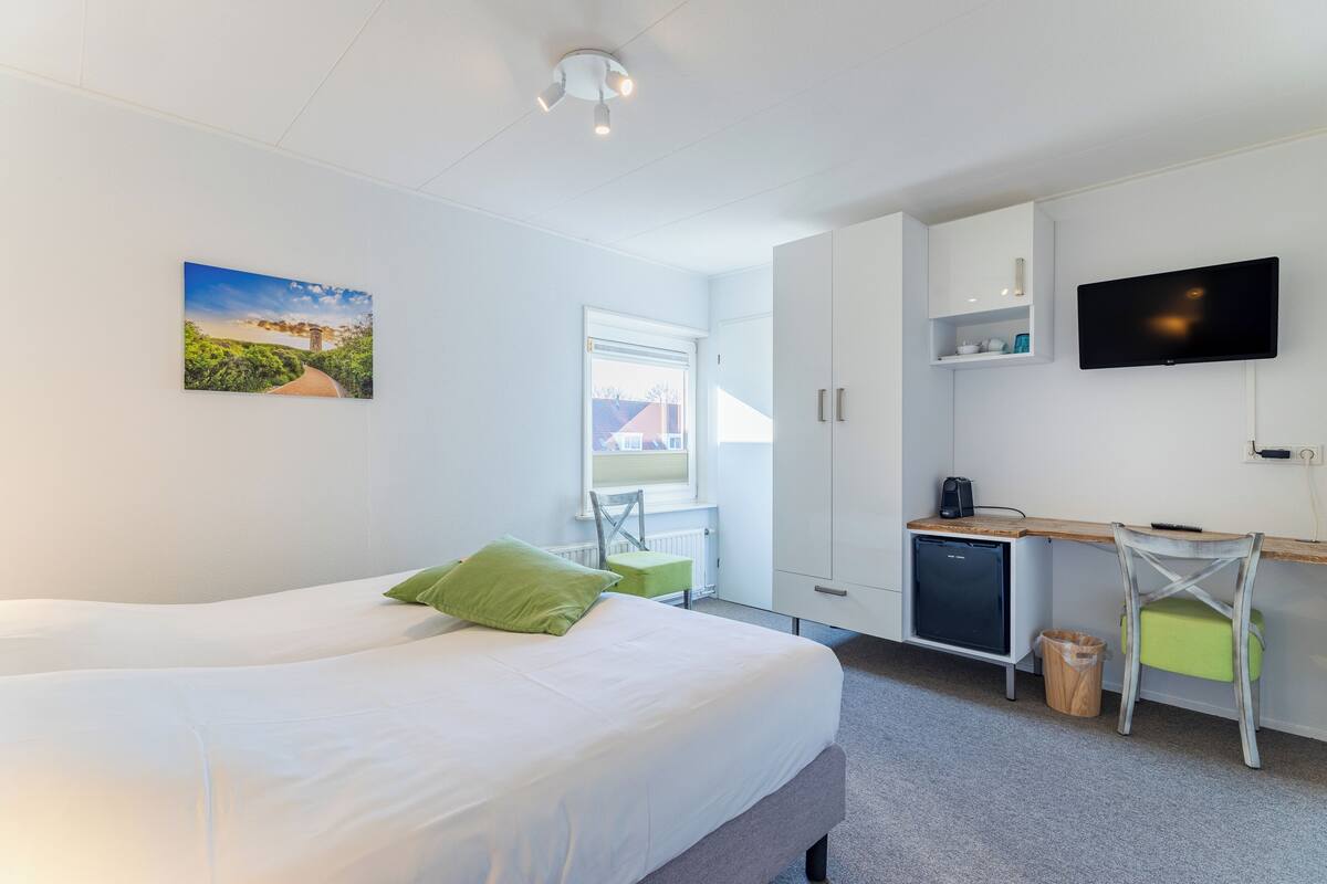 A modern hotel room with a bed, a desk, a television, and a window.