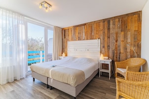 Ein Schlafzimmer mit einem Bett, Nachttischen, einem Sessel, einer Holzwand und einem Fenster.