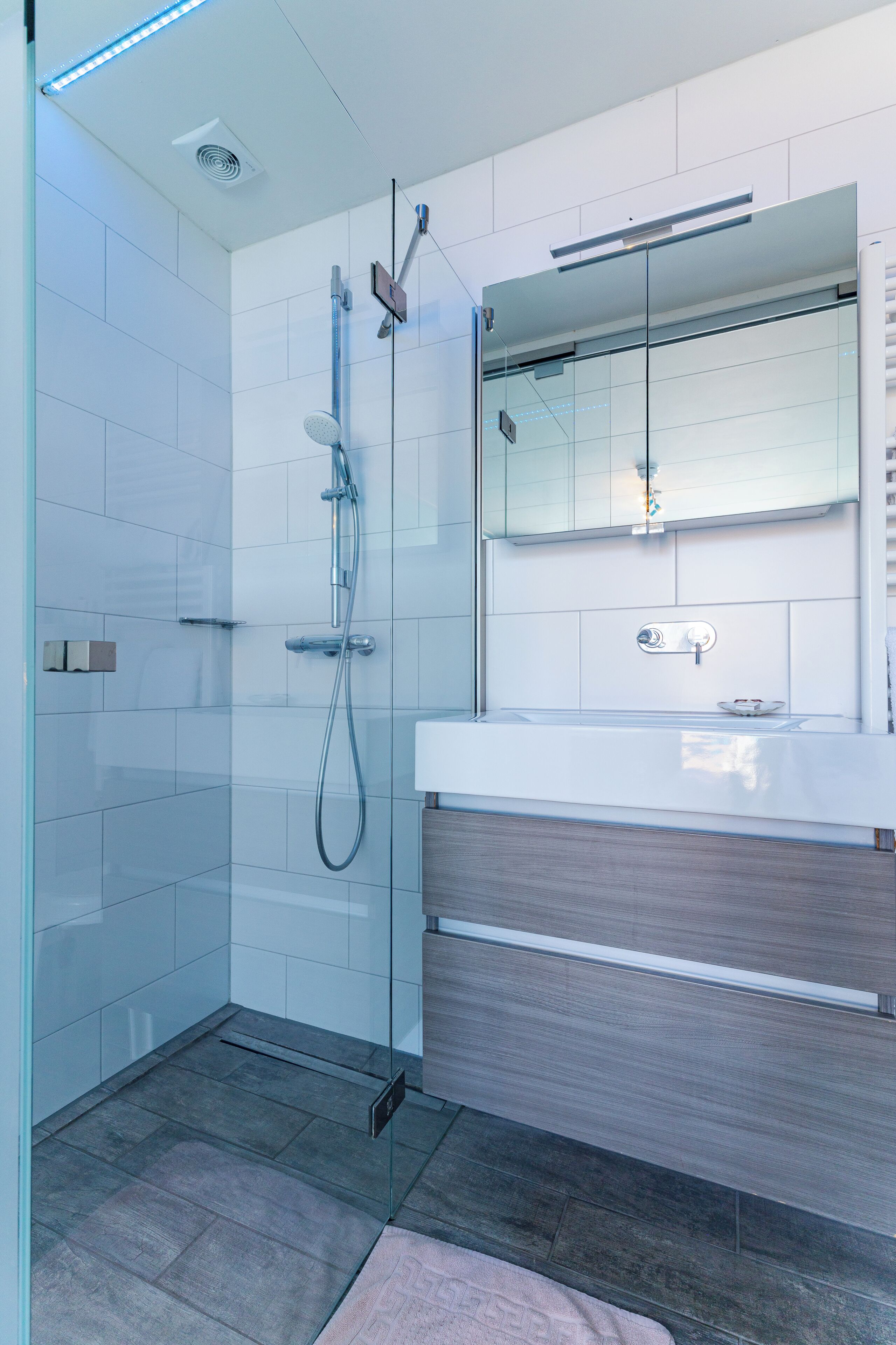 A modern bathroom with a glass shower enclosure, a white vanity with a mirror, and a wooden floor.