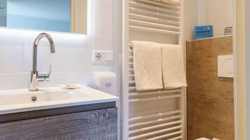 A modern bathroom with a sink, mirror, towel rack, shower, and toilet.