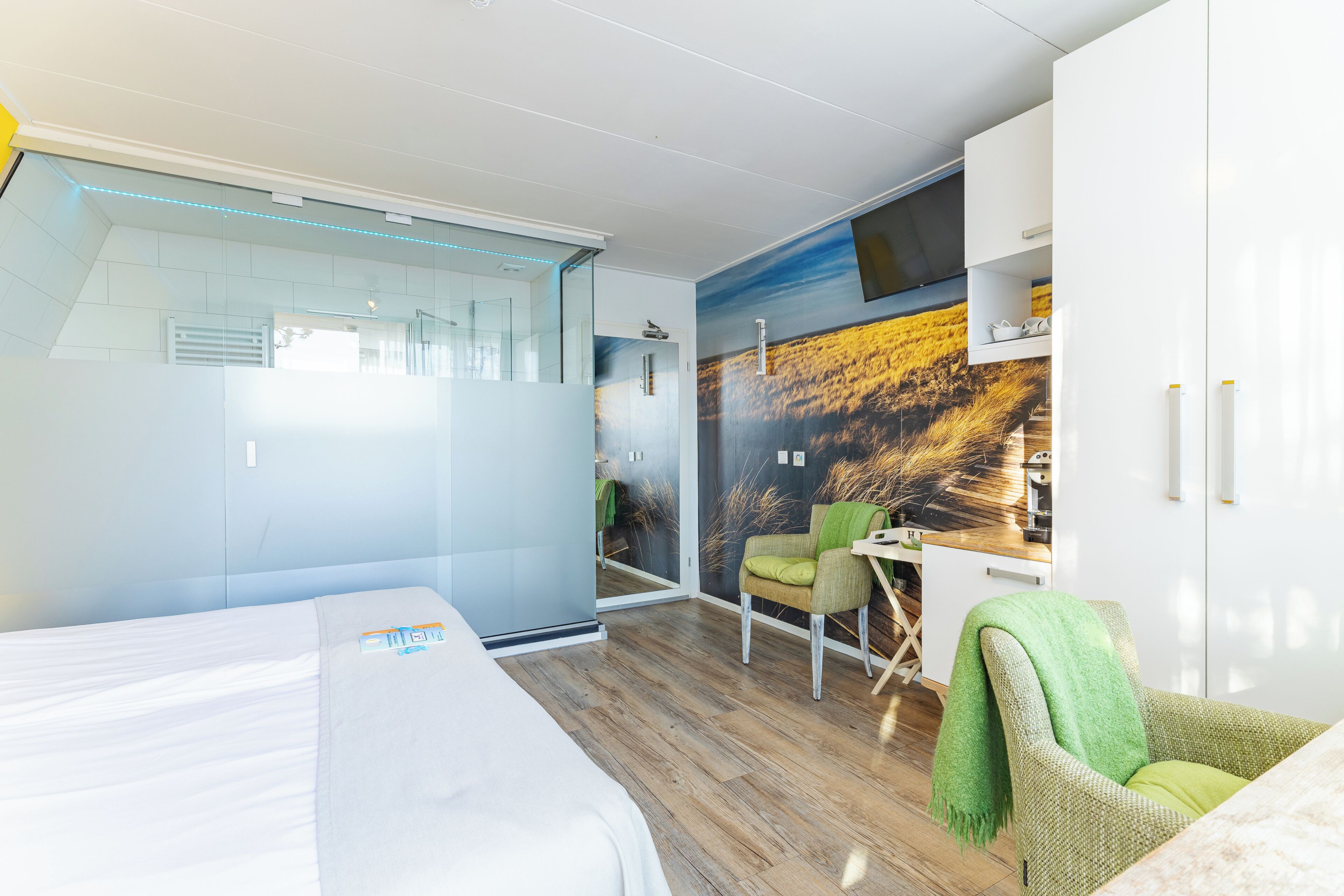 A modern hotel room with a bed, a desk, a chair, and a large window.