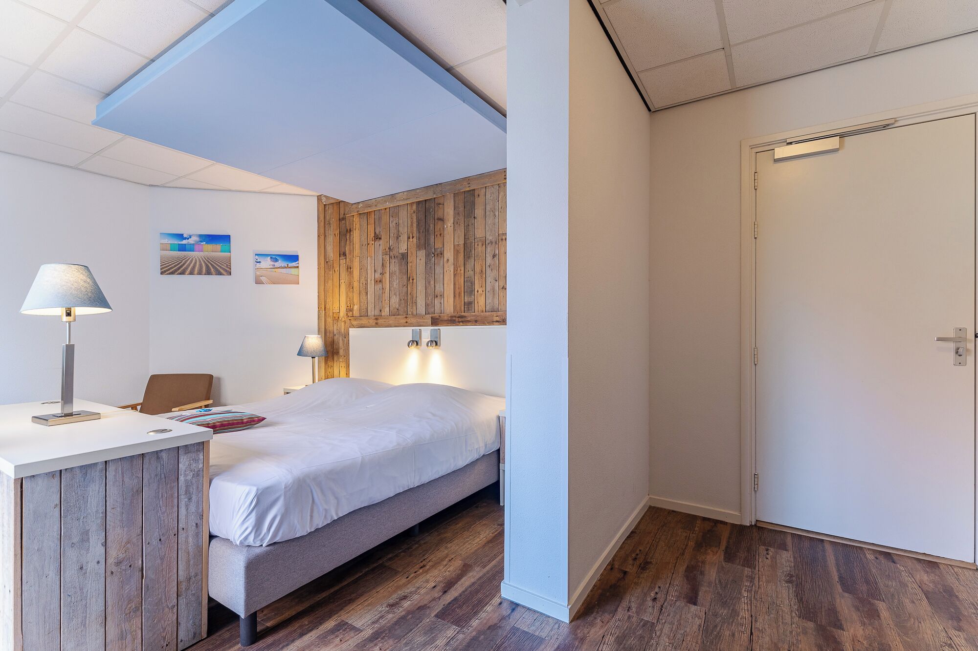 Un dormitorio con cama, mesita de noche, lámpara y pared de paneles de madera.
