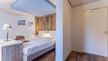 Un dormitorio con cama, mesita de noche, lámpara y pared de paneles de madera.