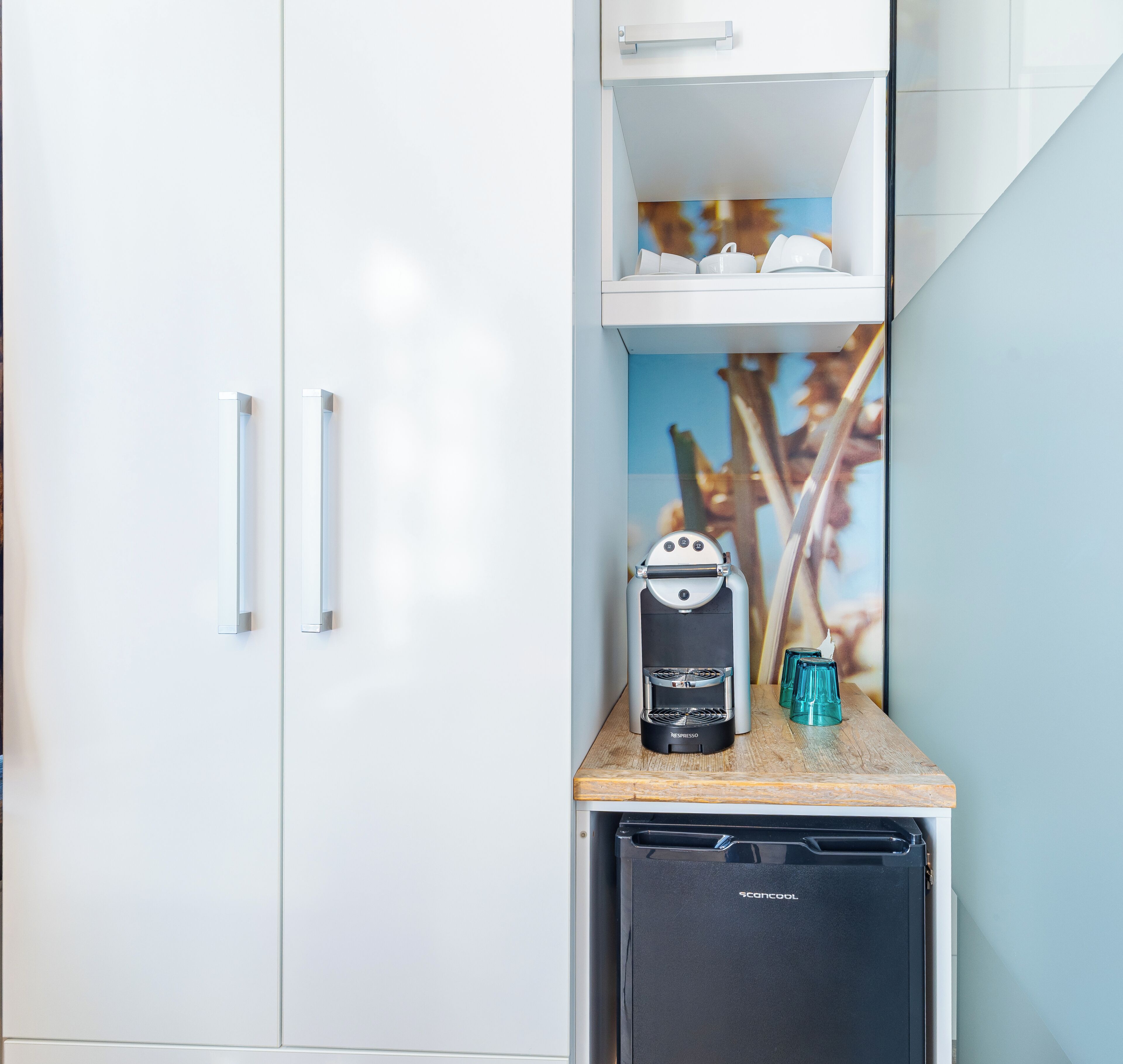 Una kitchenette con cafetera, un refrigerador pequeño y un portavasos.