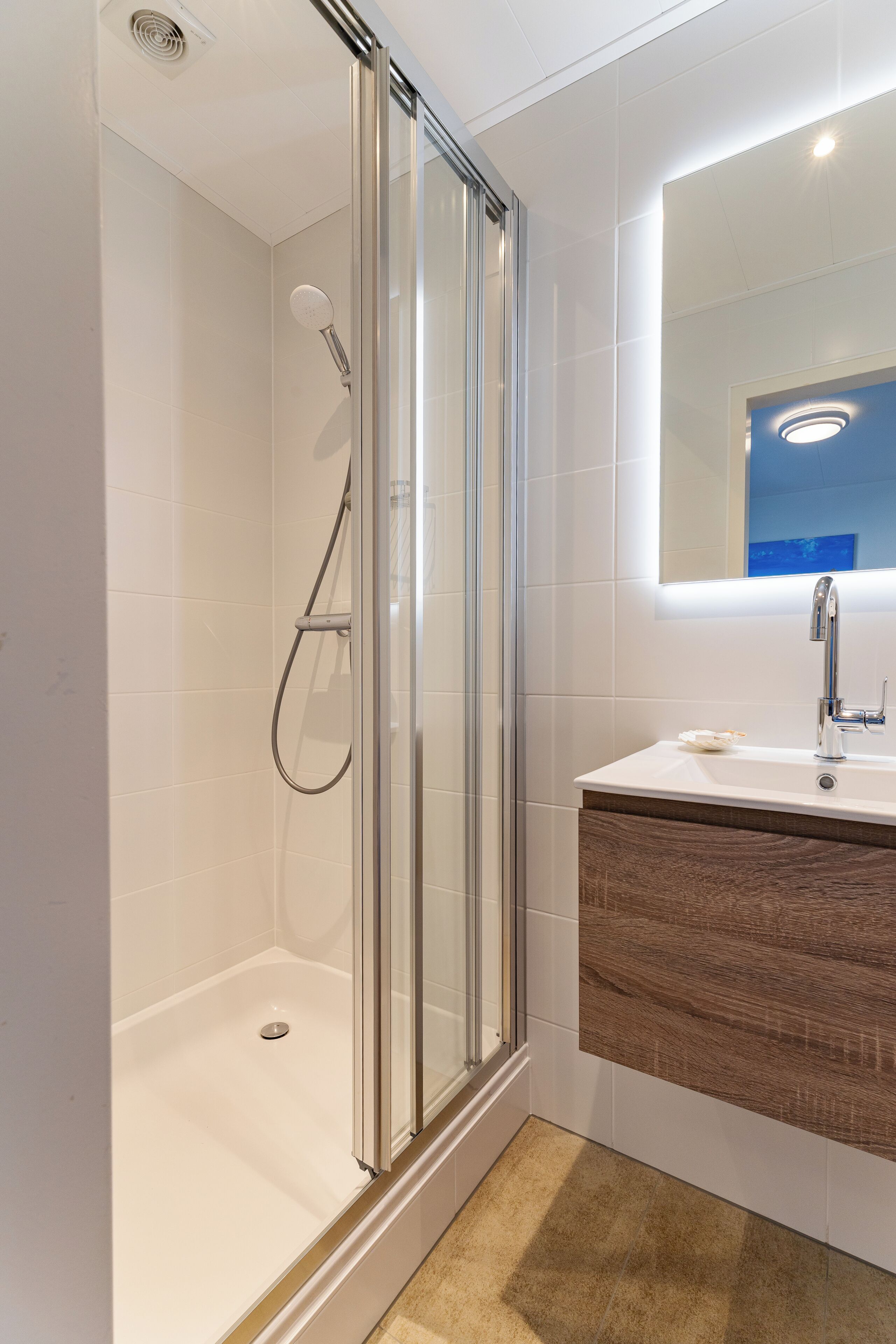 A modern bathroom with a glass-enclosed shower, a white sink, and a wooden vanity.