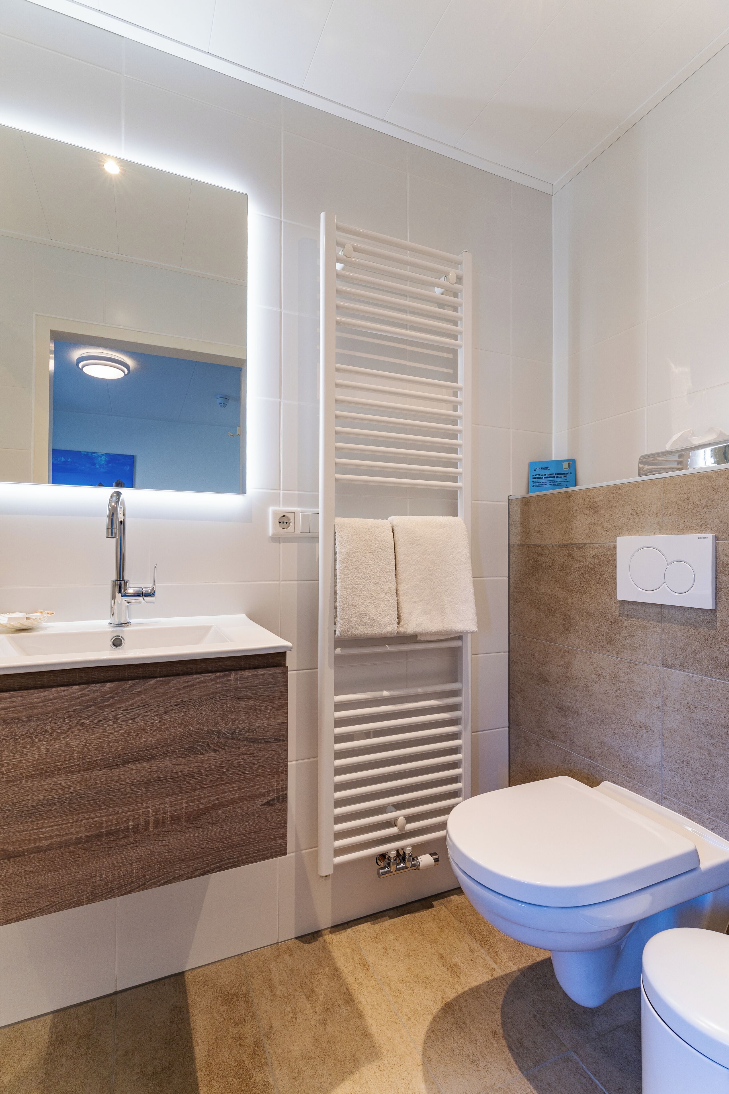 Ein modernes Badezimmer mit einem weißen Waschbecken, einem Spiegel, einem Handtuchhalter und einer Toilette.