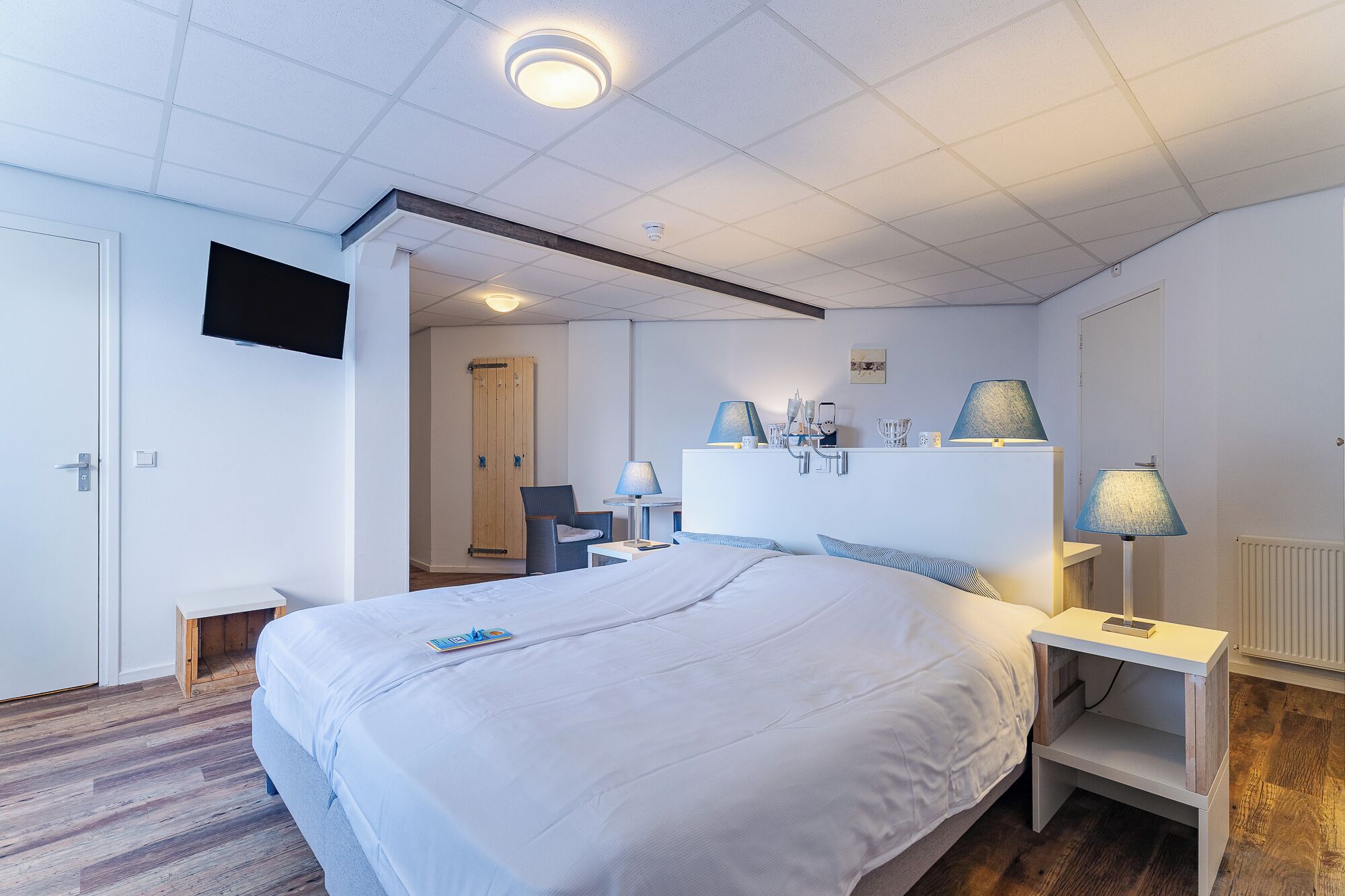 Habitación de hotel con cama, mesitas de noche, escritorio, una silla, televisor montado en la pared y un armario de madera.